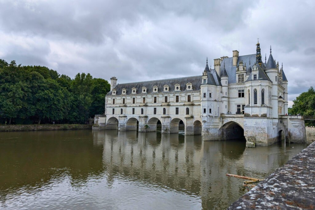 Elegant Château de Chenonceau spans the River Cher in the Loire Valley, surrounded by lush forest and reflections.