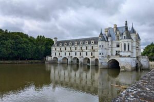 Elegant Château de Chenonceau spans the River Cher in the Loire Valley, surrounded by lush forest and reflections.