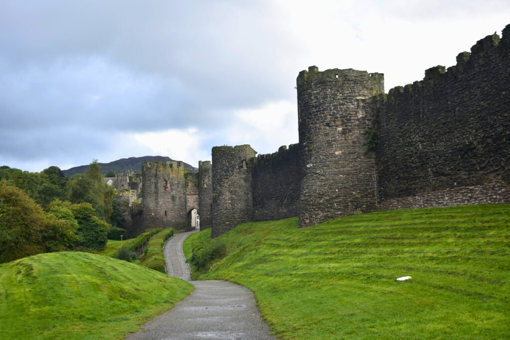 Rain-wet path leading to Conwy Castle walls in lush green Wales under brooding clouds.