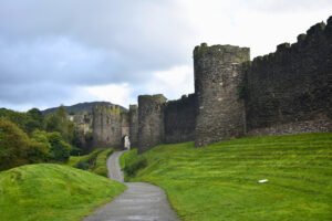 Rain-wet path leading to Conwy Castle walls in lush green Wales under brooding clouds.