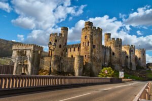 Stone towers of Conwy Castle beside the historic suspension bridge under blue skies in Conwy, Wales.