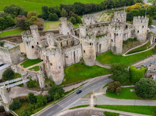 Drone view of Conwy Castle and suspension bridge in Conwy, Wales, with rugged towers and green ramparts.