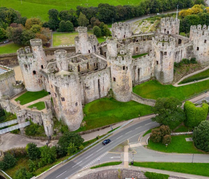 Drone view of Conwy Castle and suspension bridge in Conwy, Wales, with rugged towers and green ramparts.
