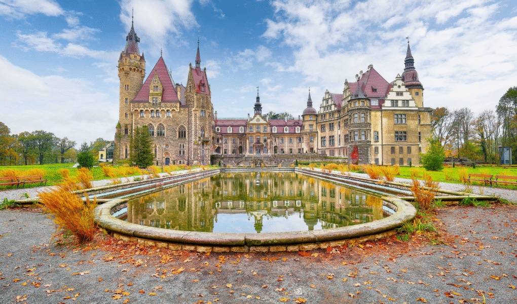 Moszna Castle reflected in pond under blue sky in autumn.