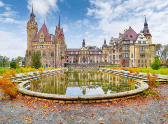 Moszna Castle reflected in pond under blue sky in autumn.