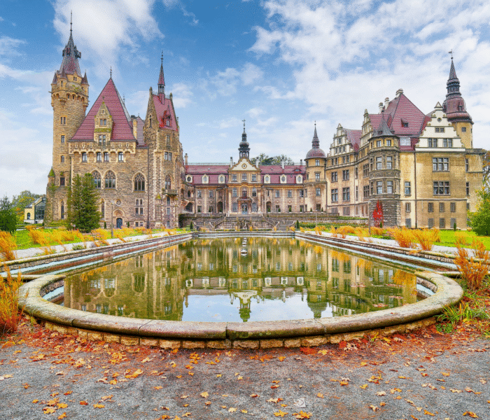 Moszna Castle reflected in pond under blue sky in autumn.