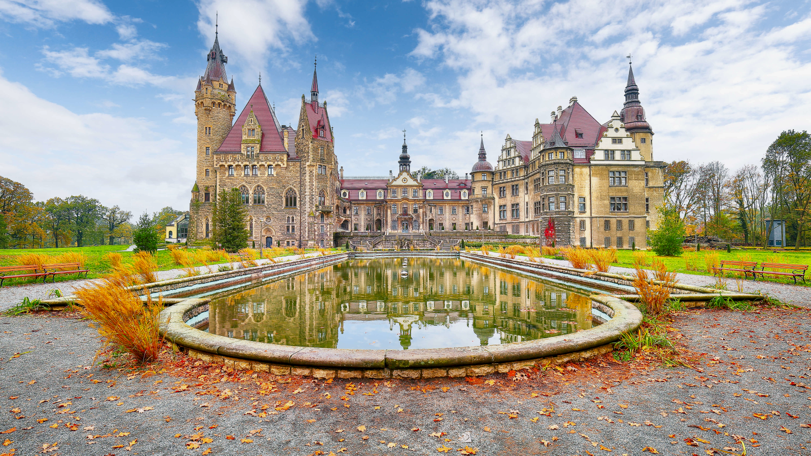 Moszna Castle reflected in pond under blue sky in autumn.