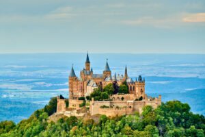 Hohenzollern Castle perched on a hill amidst forest, historic German castle dominates landscape view.