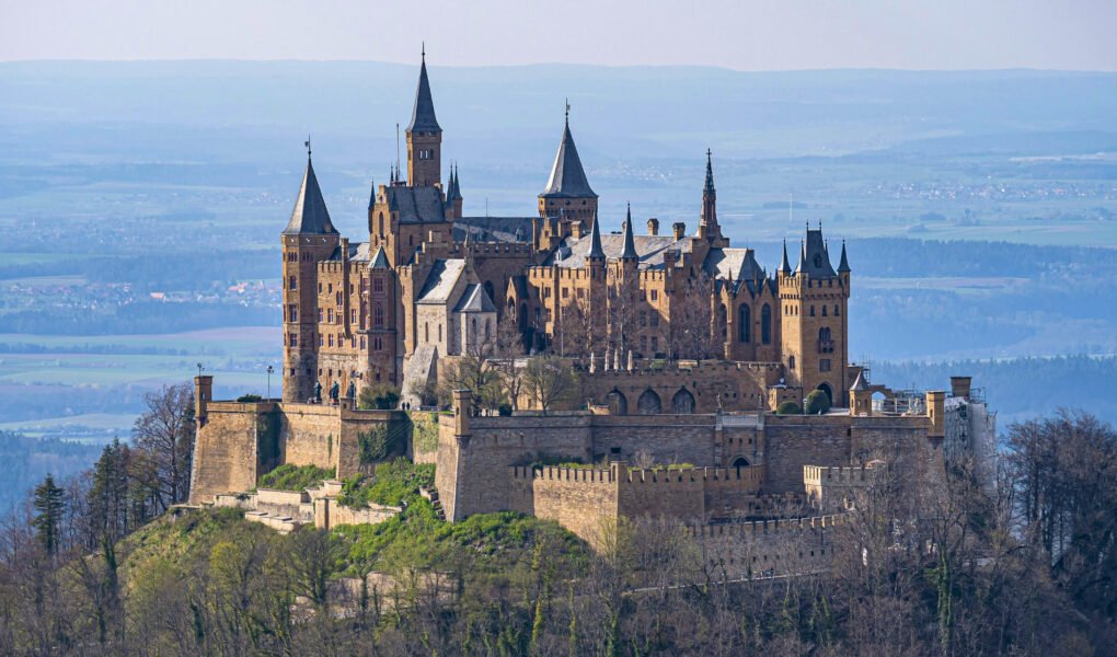 Hohenzollern Castle stands majestically atop a wooded hill in Germany, surrounded by lush scenery.