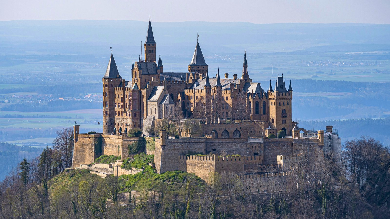 Hohenzollern Castle stands majestically atop a wooded hill in Germany, surrounded by lush scenery.