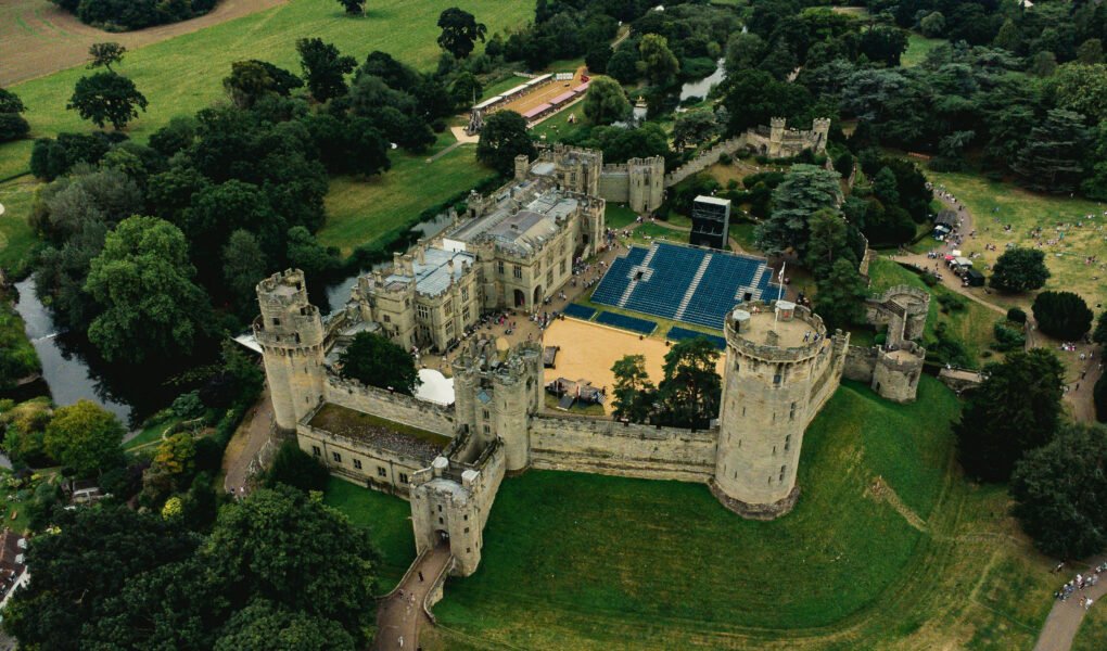 Aerial view of Warwick Castle, historic medieval fortress surrounded by lush greenery.