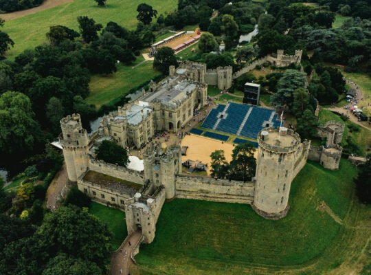 Aerial view of Warwick Castle, historic medieval fortress surrounded by lush greenery.