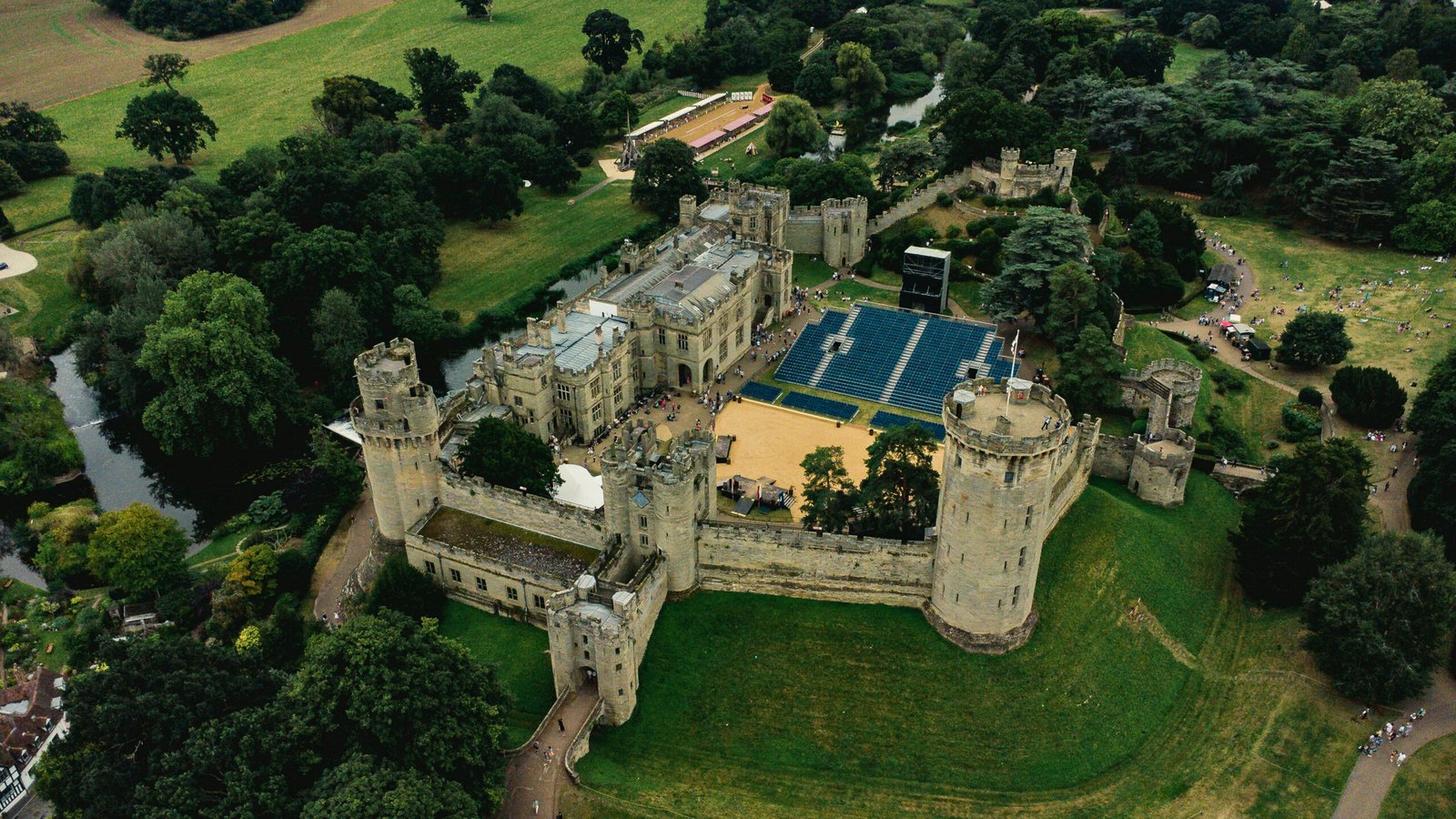 Aerial view of Warwick Castle, historic medieval fortress surrounded by lush greenery.