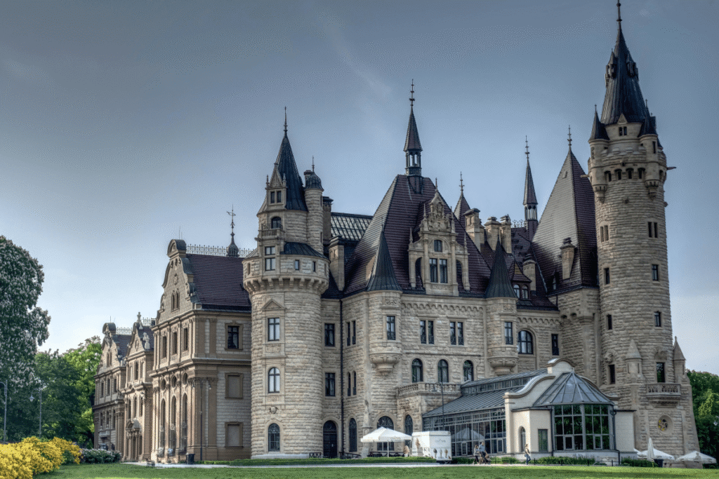 Moszna Castle in Poland with dramatic turrets and gardens on a sunny day.