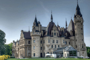 Moszna Castle in Poland with dramatic turrets and gardens on a sunny day.