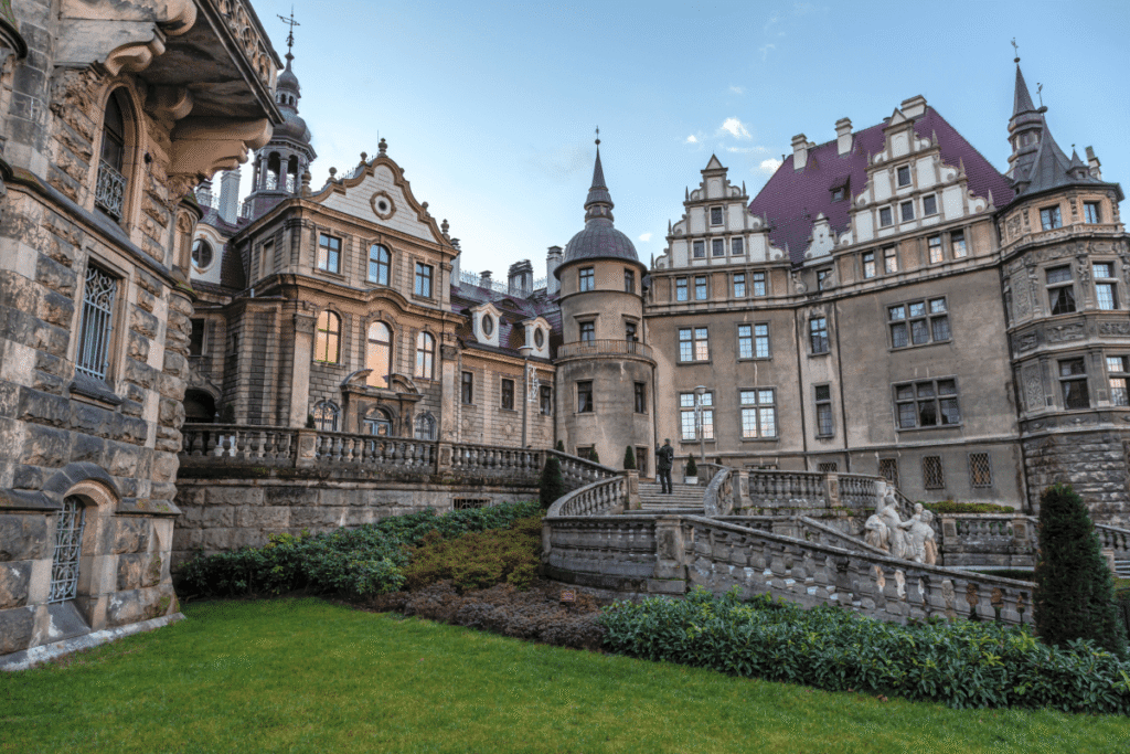 Moszna Castle grand architecture with lush gardens and ornate staircases in Poland, fairytale castle entrance view.