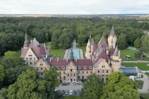 Aerial view of Moszna Castle with red roofs and lush green forest surroundings