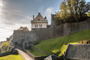 Stirling Castle fortress with stone walls and scenic grounds under a blue sky.