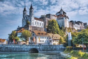 Aarburg Castle perched above riverside town and stone bridge under blue sky