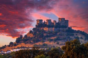 Almodovar Castle silhouetted on hill under dramatic pink-orange sunset sky