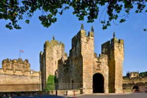 Alnwick Castle stone gatehouse and towers under blue sky