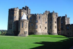 Alnwick Castle exterior with round towers and manicured lawn under blue sky