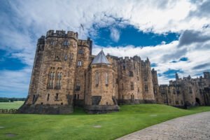 Stone towers of Alnwick Castle against cloudy blue sky