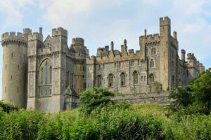 Arundel Castle's flint walls and towers rising above greenery in West Sussex, England, under a bright sky.