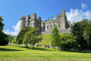 Arundel Castle in West Sussex seen from lawns with trees under a bright blue summer sky.