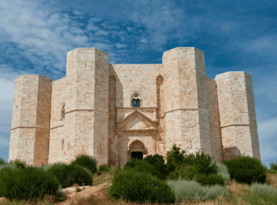 Castel del Monte’s octagonal towers rising above Apulia scrub under a bright blue sky in Italy.