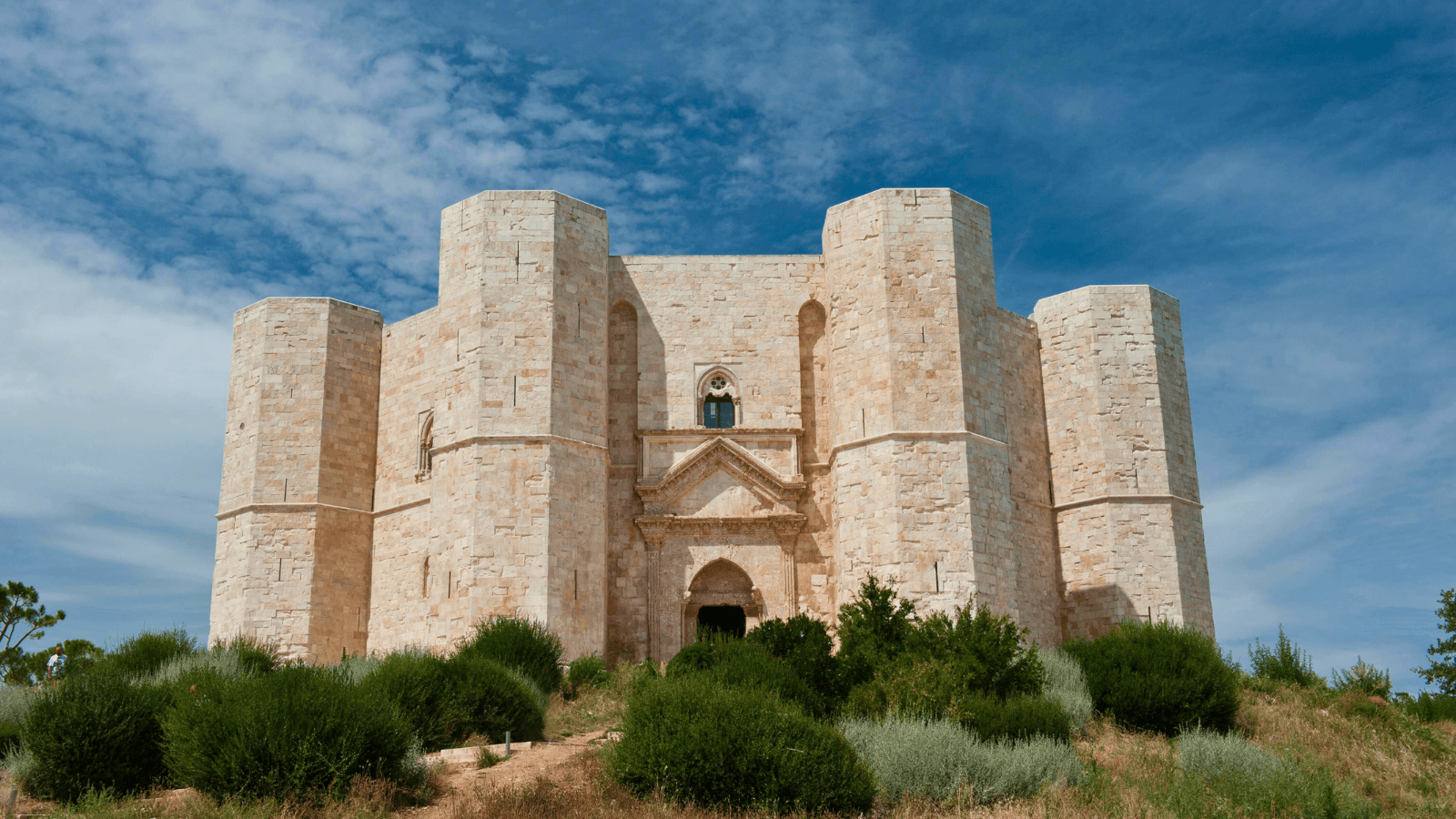 Castel del Monte’s octagonal towers rising above Apulia scrub under a bright blue sky in Italy.