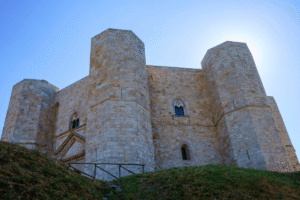 Castel del Monte’s pale stone towers under bright sky in Apulia, Italy, seen from the grassy slope.