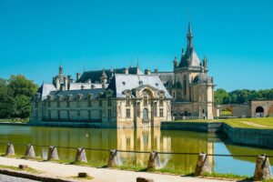 Chantilly Castle reflected in calm moat under blue sky