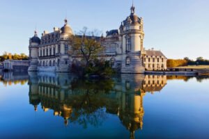 Chantilly Castle reflected in calm moat with autumn trees and clear sky