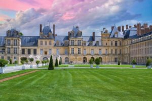 Façade of Fontainebleau Palace with manicured lawn under pink-purple sunset sky