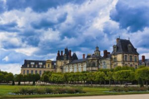 Château de Fontainebleau facade under dramatic clouds, trimmed gardens in front