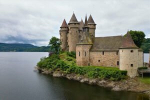 Chateau de Val towers beside serene lake and green shoreline