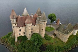 Aerial view of Chateau de Val on a rocky island surrounded by calm lake water