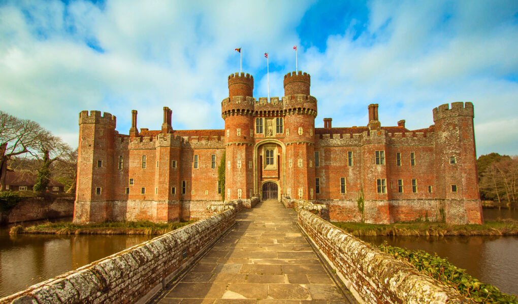 Stone bridge to Herstmonceux Castle, a moated red-brick fortress under bright skies in East Sussex, England.