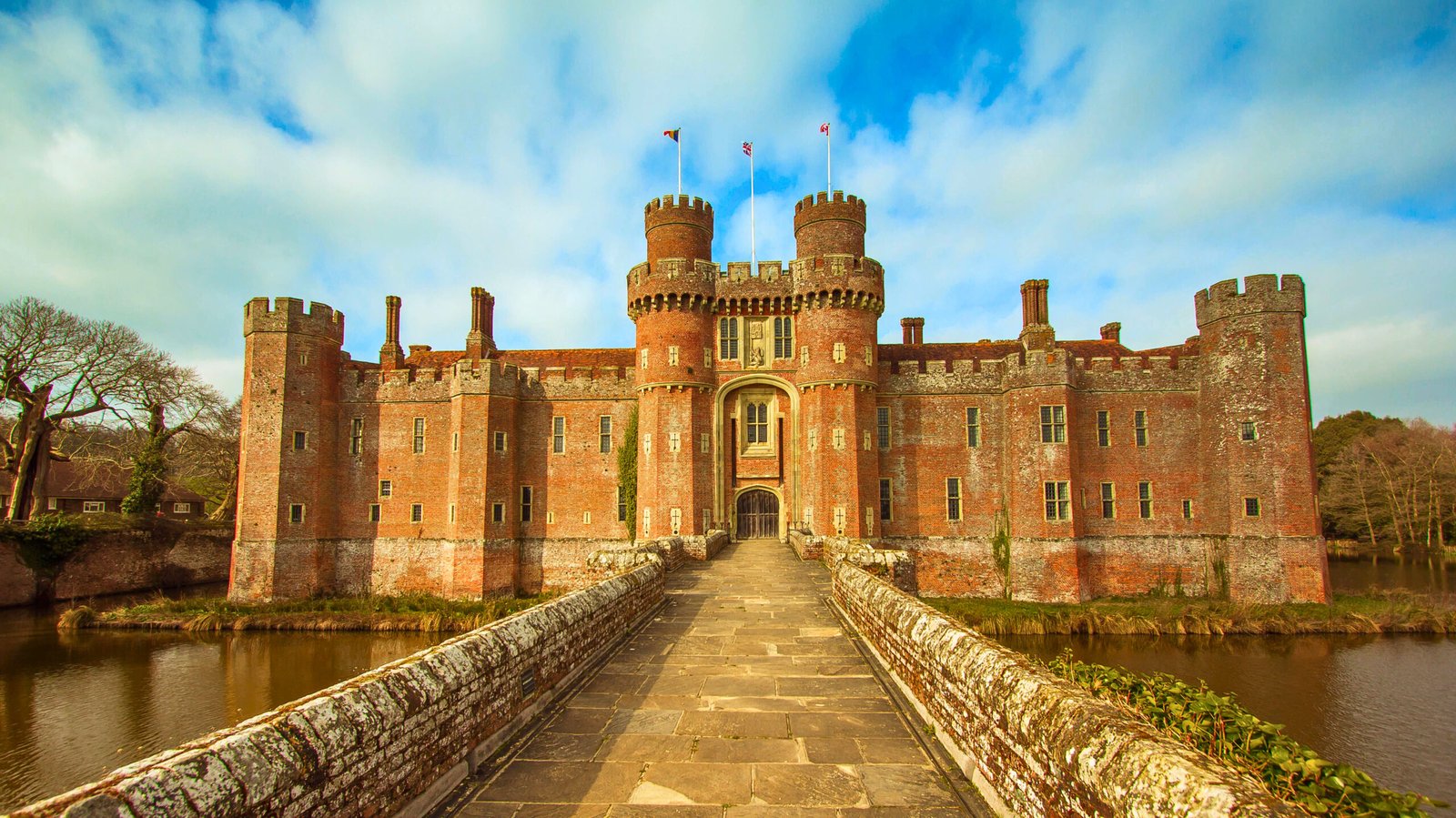 Stone bridge to Herstmonceux Castle, a moated red-brick fortress under bright skies in East Sussex, England.