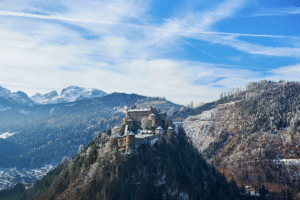 Hohenwerfen Castle perched on snowy cliff in Werfen, Austria, surrounded by alpine mountains and winter forest.