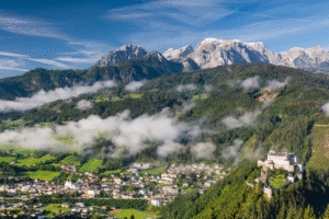 Panoramic view of Hohenwerfen Fortress over Werfen valley, misty forests, and rugged Salzburg Alps in Austria.