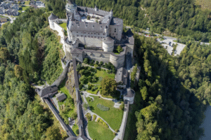 Aerial view of Hohenwerfen Fortress perched above forested valley and gardens in Werfen, Austria.