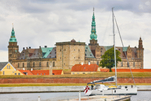 Kronborg Castle in Helsingør Denmark with sailboat and moat under cloudy sky.