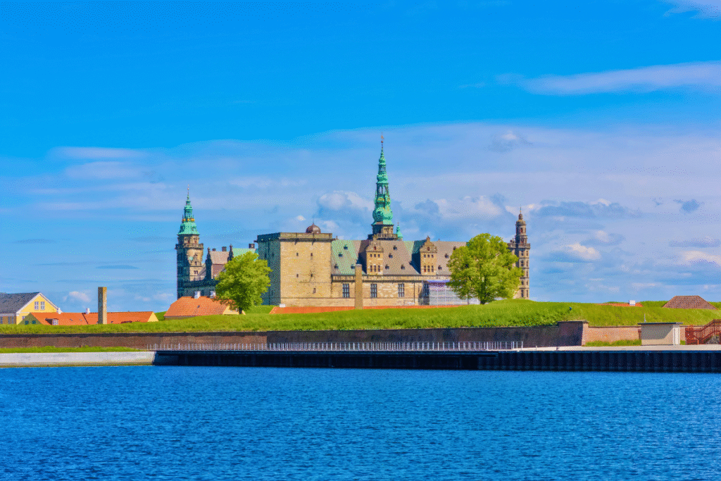 Kronborg Castle above Helsingør waterfront under bright blue sky and calm water.