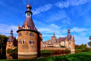 Ooidonk Castle with round towers reflected in the moat under blue sky