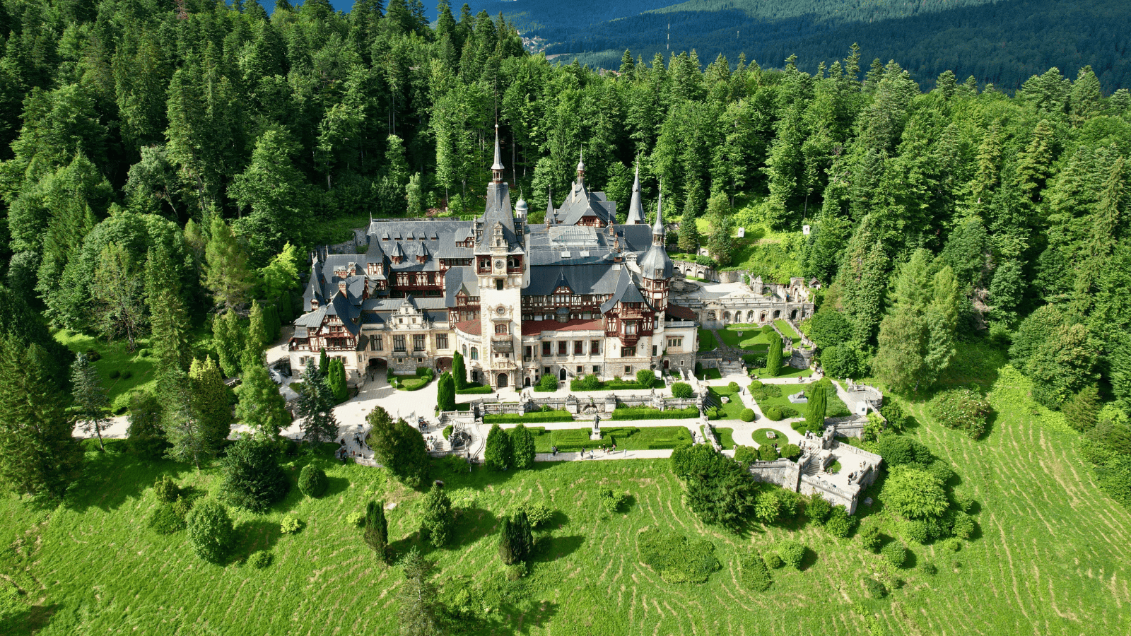 Aerial view of Peleș Castle in Sinaia, Romania, surrounded by forested Carpathian mountains and landscaped gardens.