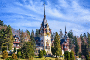Peleș Castle in Sinaia, Romania, framed by evergreens beneath a bright blue sky in the Carpathians.