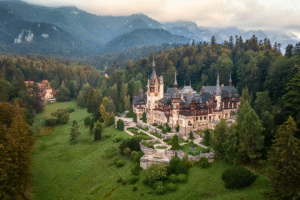 Aerial view of Peleș Castle in Sinaia, Romania, surrounded by Carpathian forests and misty mountains.
