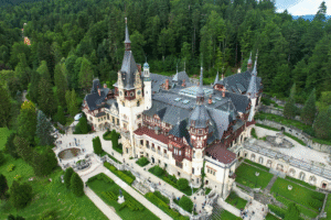 Aerial view of Peleș Castle in Sinaia, Romania, surrounded by lush forest and manicured gardens.